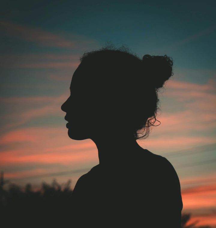 Silhouette of a woman with a bun against a vibrant sunset sky