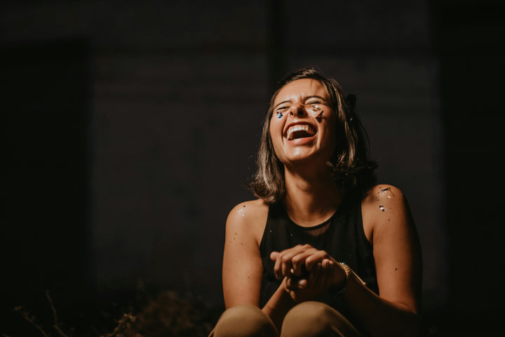 A woman sits in a dimly lit space, wearing a sleeveless top